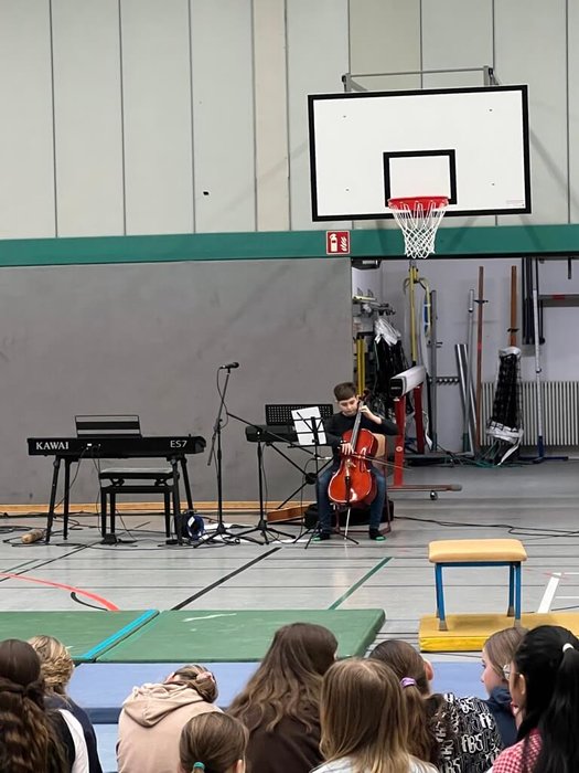 Ein Schüler sitzt auf einem Stuhl und spielt ein Streichinstrument