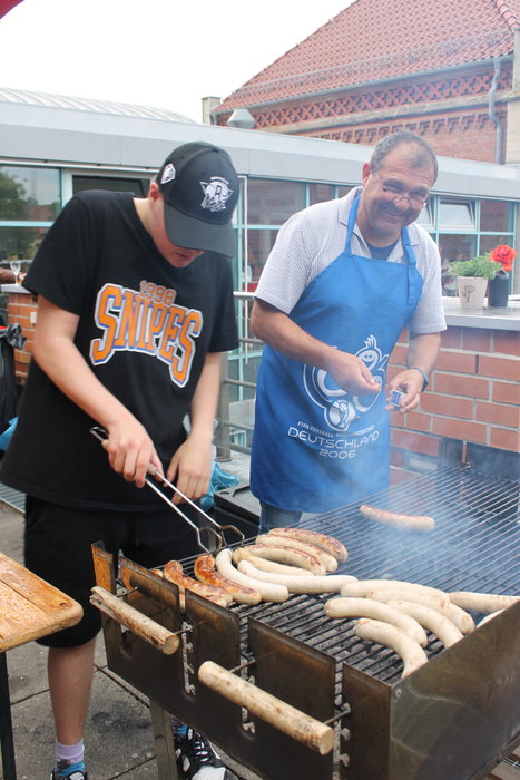 Zwei Männer mit Schürzen grillen Würstchen