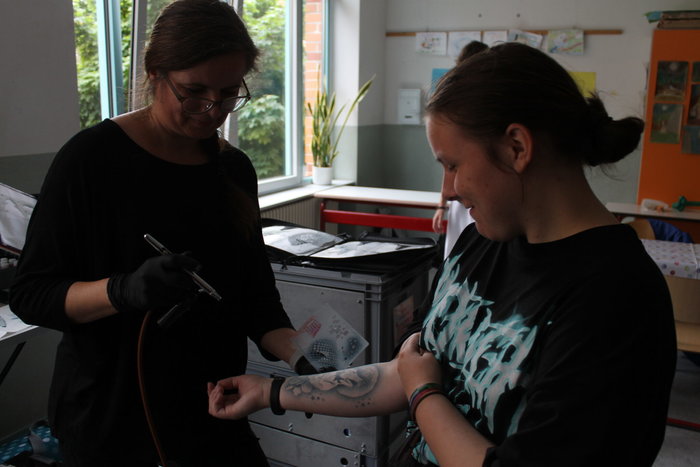 Eine Frau sprayt einem Mädchen ein Airbrush-Tattoo