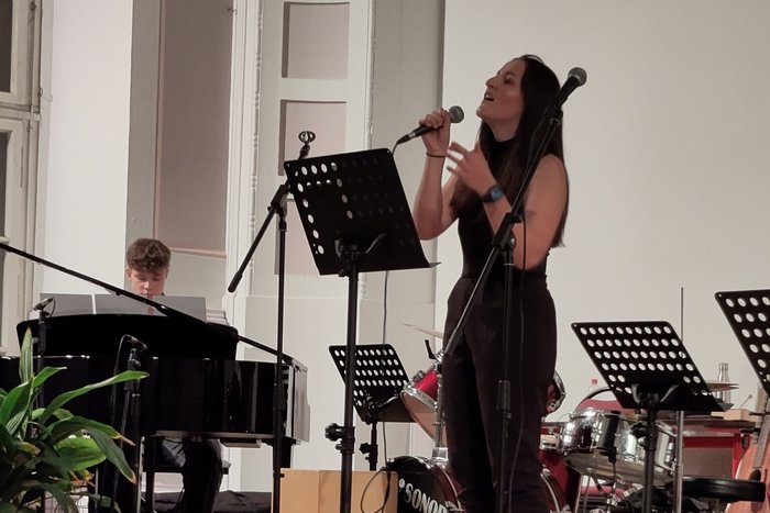 Die Musiklehrerin trägt in Begleitung von einem Klavier ein Stück vor.